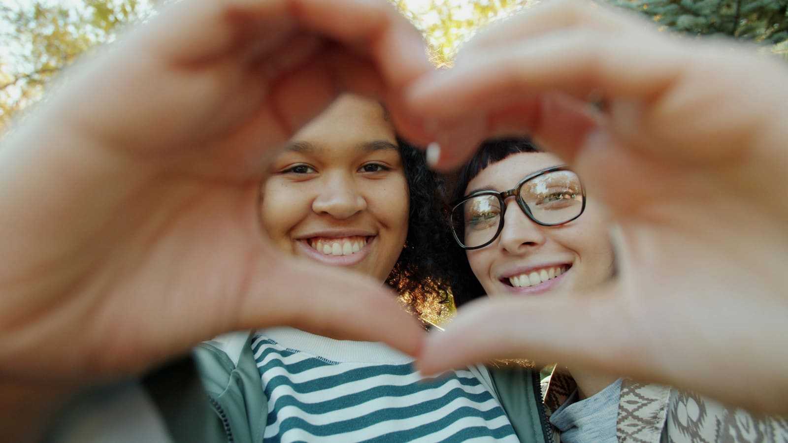 Two friends forming a heart shape with their hands outdoors